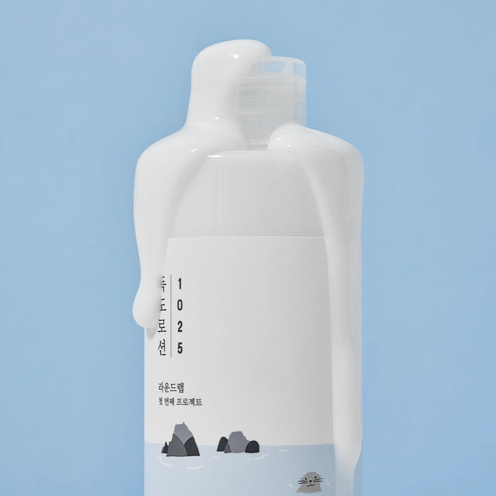 ROUND LAB's Dokdo moisturising lotion for sensitive skin and it's lightweight cream-serum texture, on a blue background